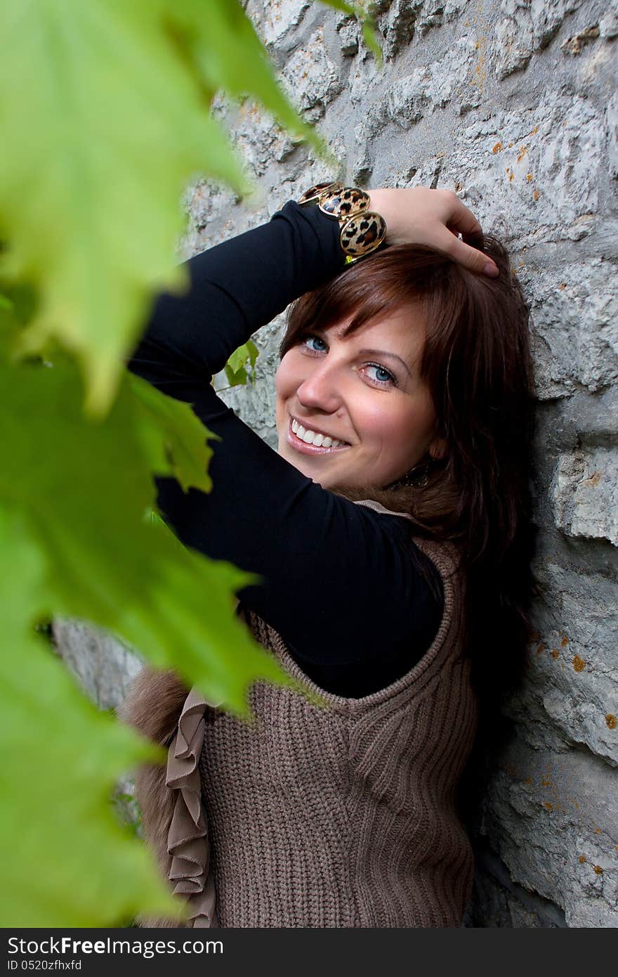 Beautiful blue-eyed smiling girl outdoors near the wall and maple. Beautiful blue-eyed smiling girl outdoors near the wall and maple