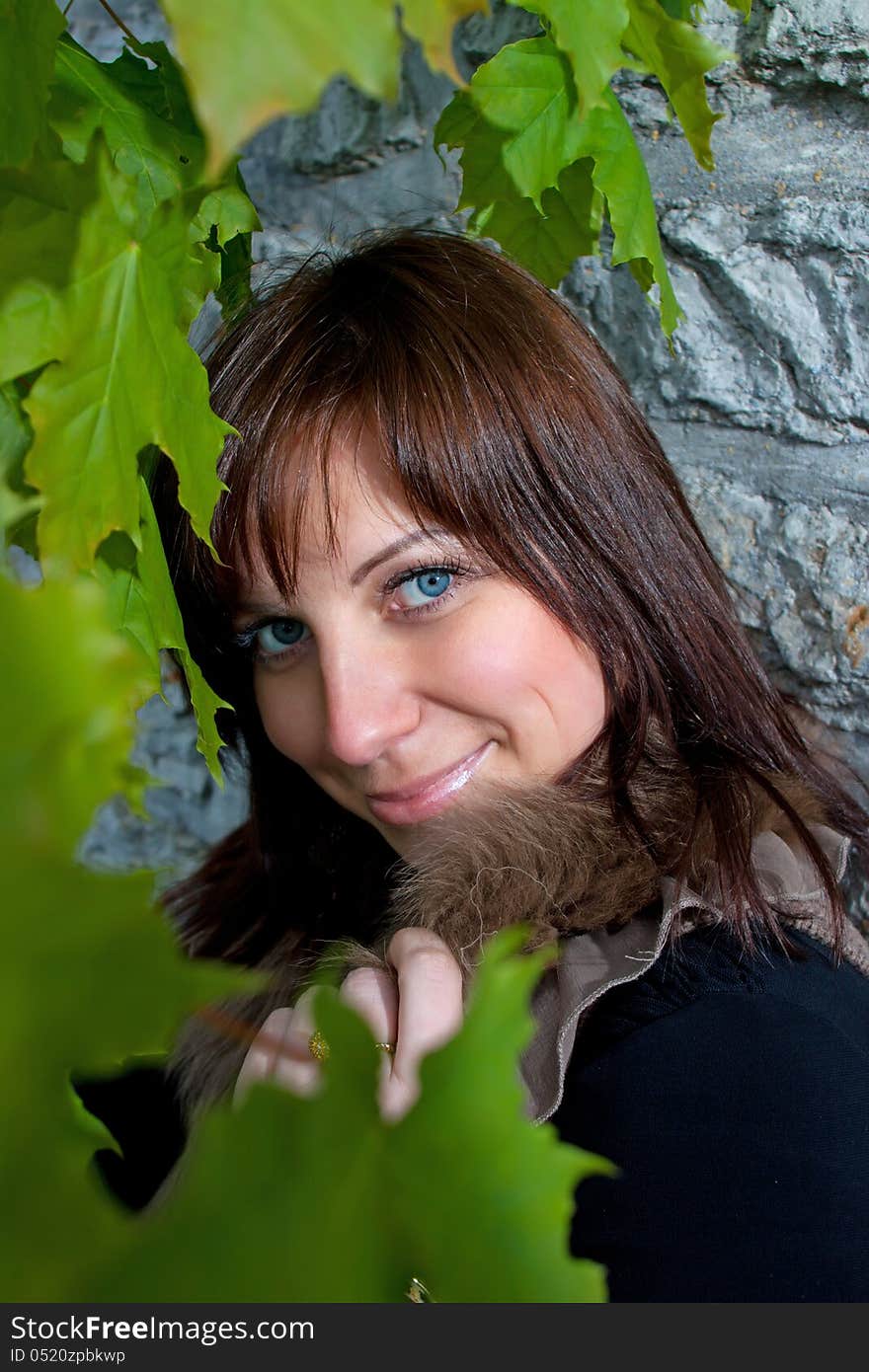 Beautiful blue-eyed smiling girl outdoors near the wall and maple. Beautiful blue-eyed smiling girl outdoors near the wall and maple