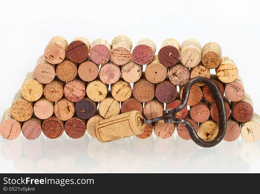 Old corkscrew with a cork on it against the stack of used wine corks with reflection in a glass table. Old corkscrew with a cork on it against the stack of used wine corks with reflection in a glass table