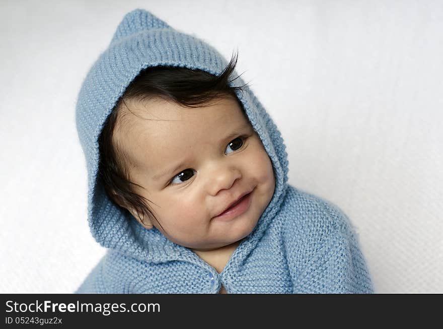 A newborn baby is wearing blue cardigan with hood smiles on a soft white background. Use the photo to represent life, parenting or childhood. A newborn baby is wearing blue cardigan with hood smiles on a soft white background. Use the photo to represent life, parenting or childhood.