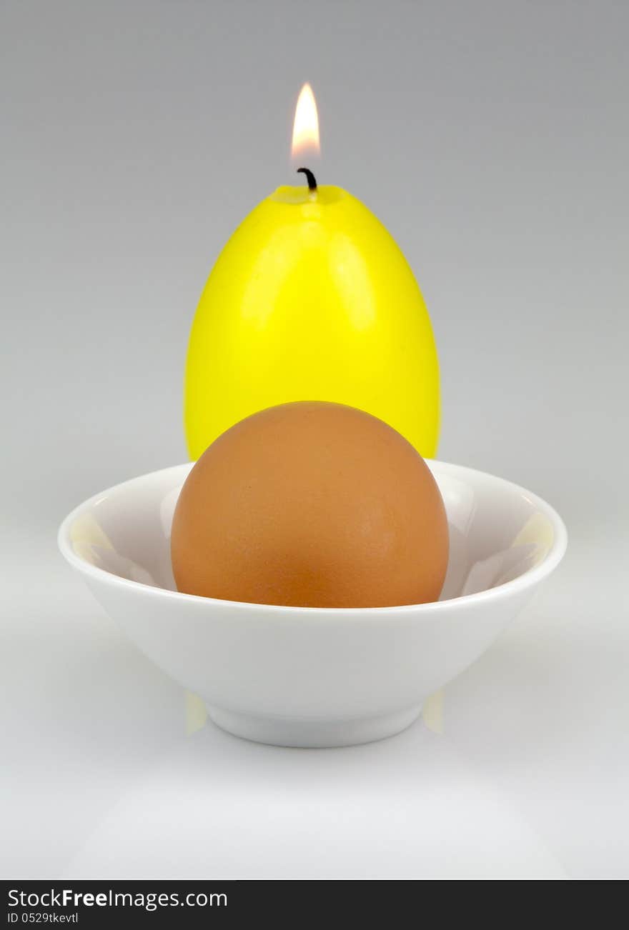 Egg in a small dish and a burning Easter candle in the form of egg. Egg in a small dish and a burning Easter candle in the form of egg