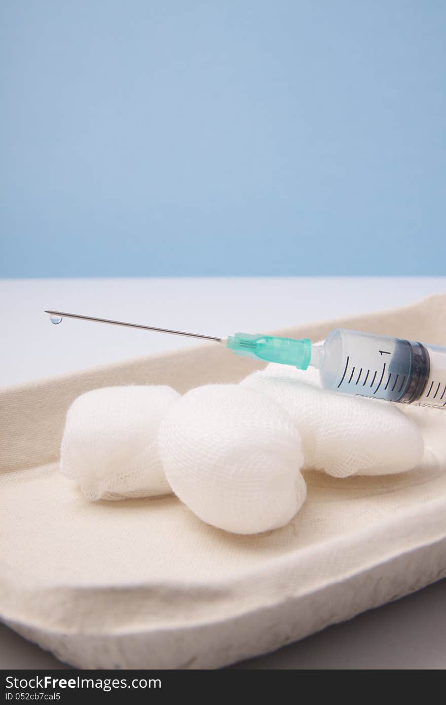 Syringe and round gauze ball.Blue background