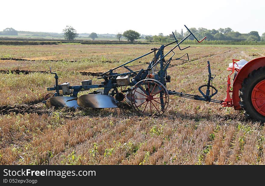 An Agricultural Tractor Pulling a Vintage Plough.