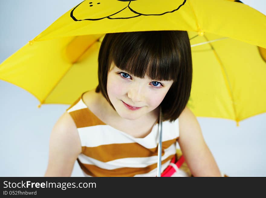 Colour portrait of a pretty young girl smiling under a fun yellow umbrella. Colour portrait of a pretty young girl smiling under a fun yellow umbrella.