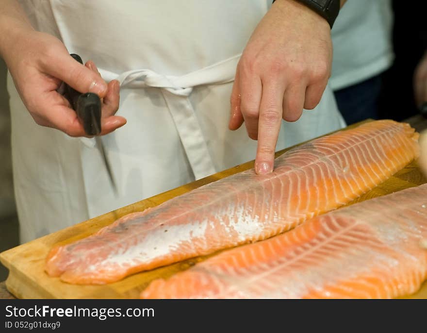 Cooks hands preparing fresh salmon fish. Image taken closeup with cooks hands testing the quality of a big piece of fresh salmon fish. Cooks hands preparing fresh salmon fish. Image taken closeup with cooks hands testing the quality of a big piece of fresh salmon fish.