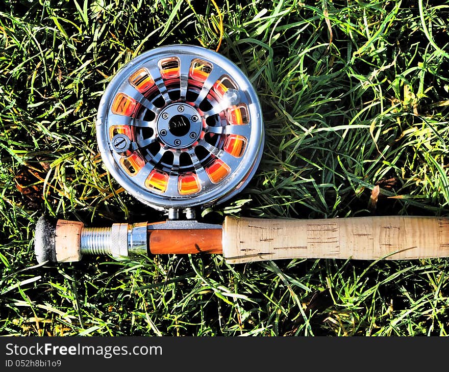 Shiny aluminium reel attached to fishing rod with cork handle on grass. Shiny aluminium reel attached to fishing rod with cork handle on grass