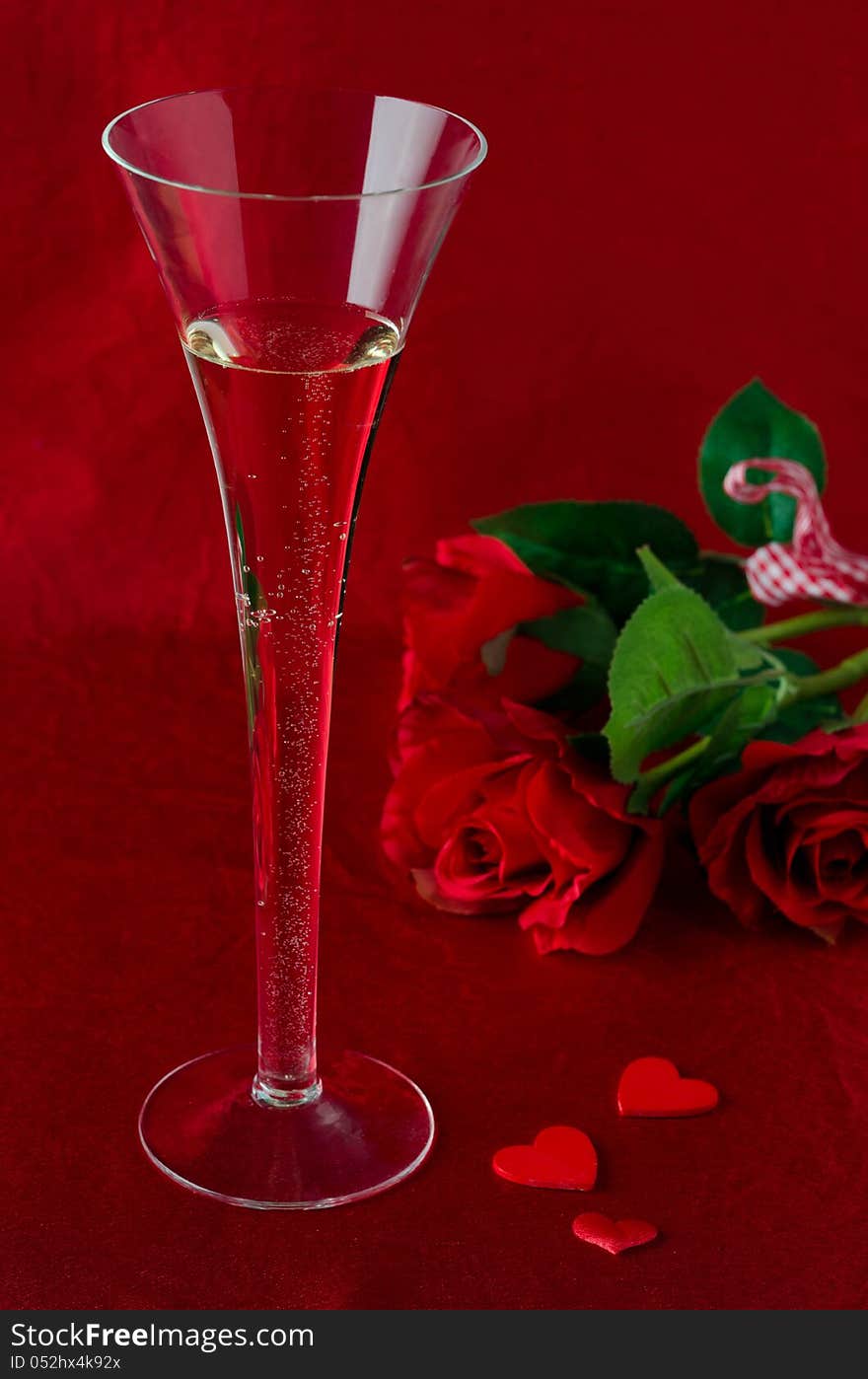 A glass of champagne and red roses for Valentine's Day on a red background. A glass of champagne and red roses for Valentine's Day on a red background