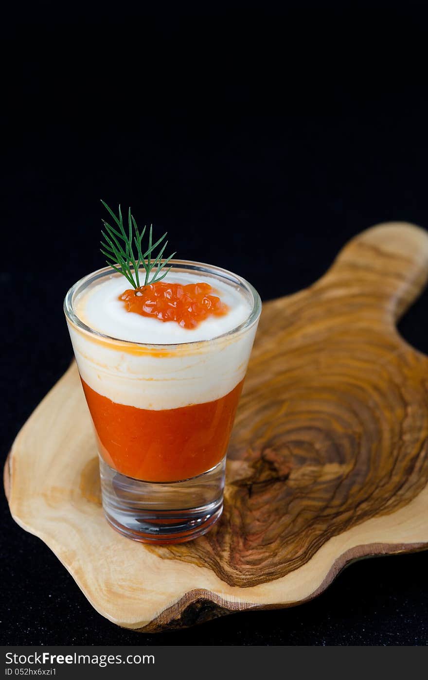 Appetizer of sweet pepper, cream and red caviar in a glasses on a wooden board on a black background