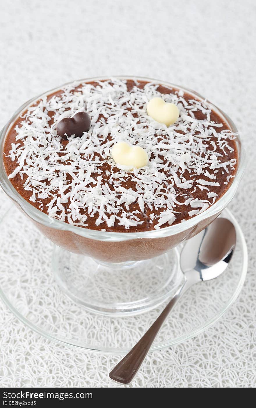 Chocolate mousse in a glass sundae dish with chocolate hearts decorated with coconut on a white background