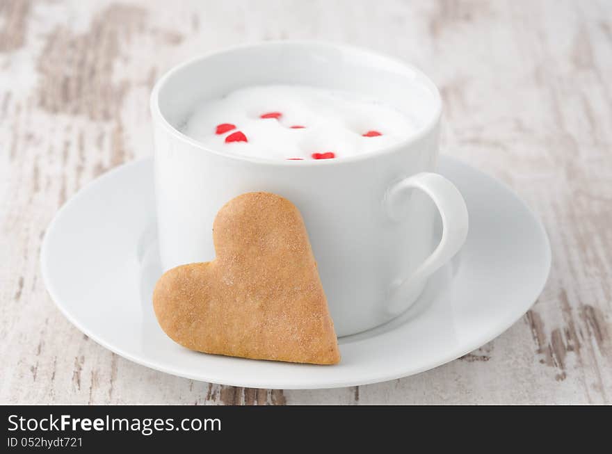 Cup of hot milk with foam, decorated with sugar hearts and heart-shaped cookies on the table