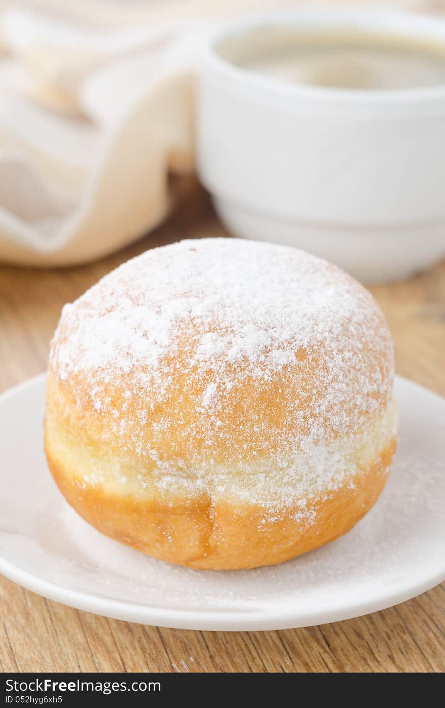 Sweet donut sprinkled with powdered sugar on a plate and cup of coffee closeup. Sweet donut sprinkled with powdered sugar on a plate and cup of coffee closeup