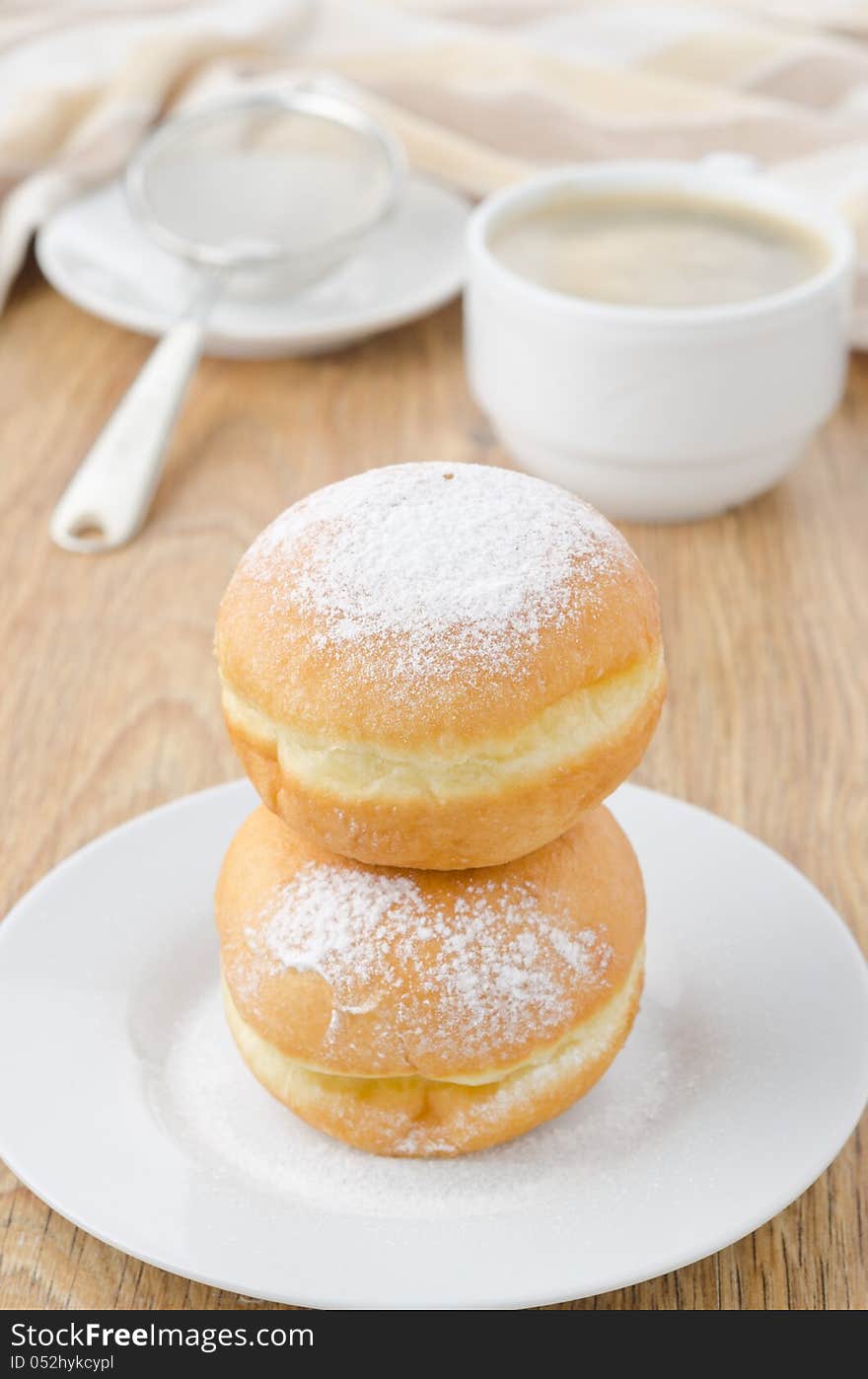 Sweet donuts sprinkled with powdered sugar on a plate and a cup of coffee. Sweet donuts sprinkled with powdered sugar on a plate and a cup of coffee