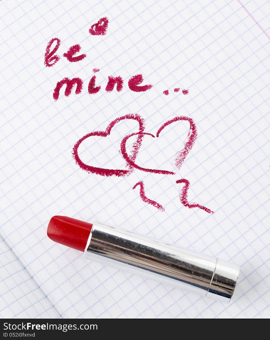 Sign on heart in a notebook and red lipstick in Valentine's Day closeup. Sign on heart in a notebook and red lipstick in Valentine's Day closeup