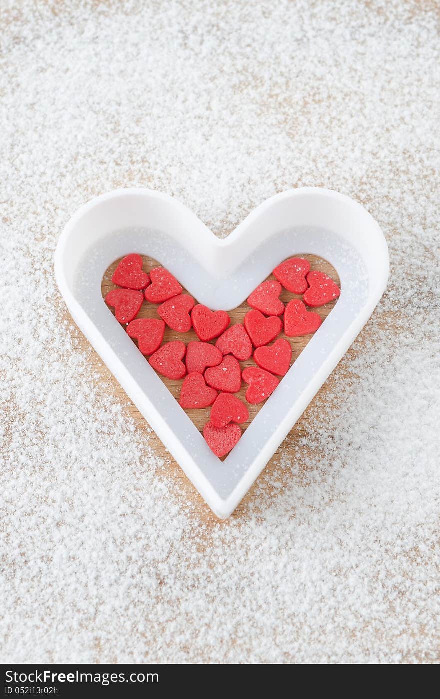 Sugar hearts in white baking dish on a board sprinkled with powdered sugar on a wooden board