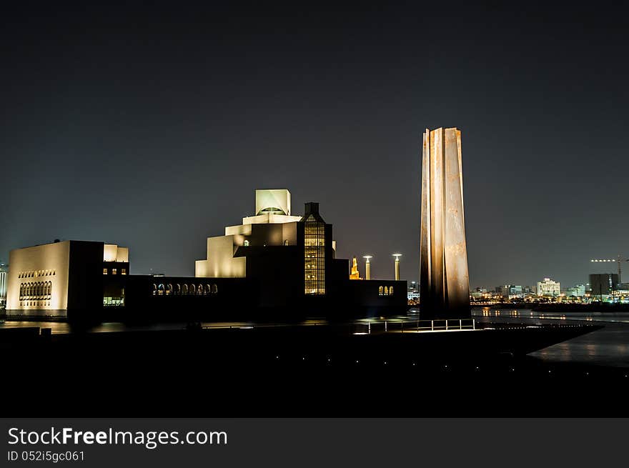 Night shot of the Doha Museum of Islamic Art, showing the strong reflections of light made by the building design and the'seven' monument on the side.