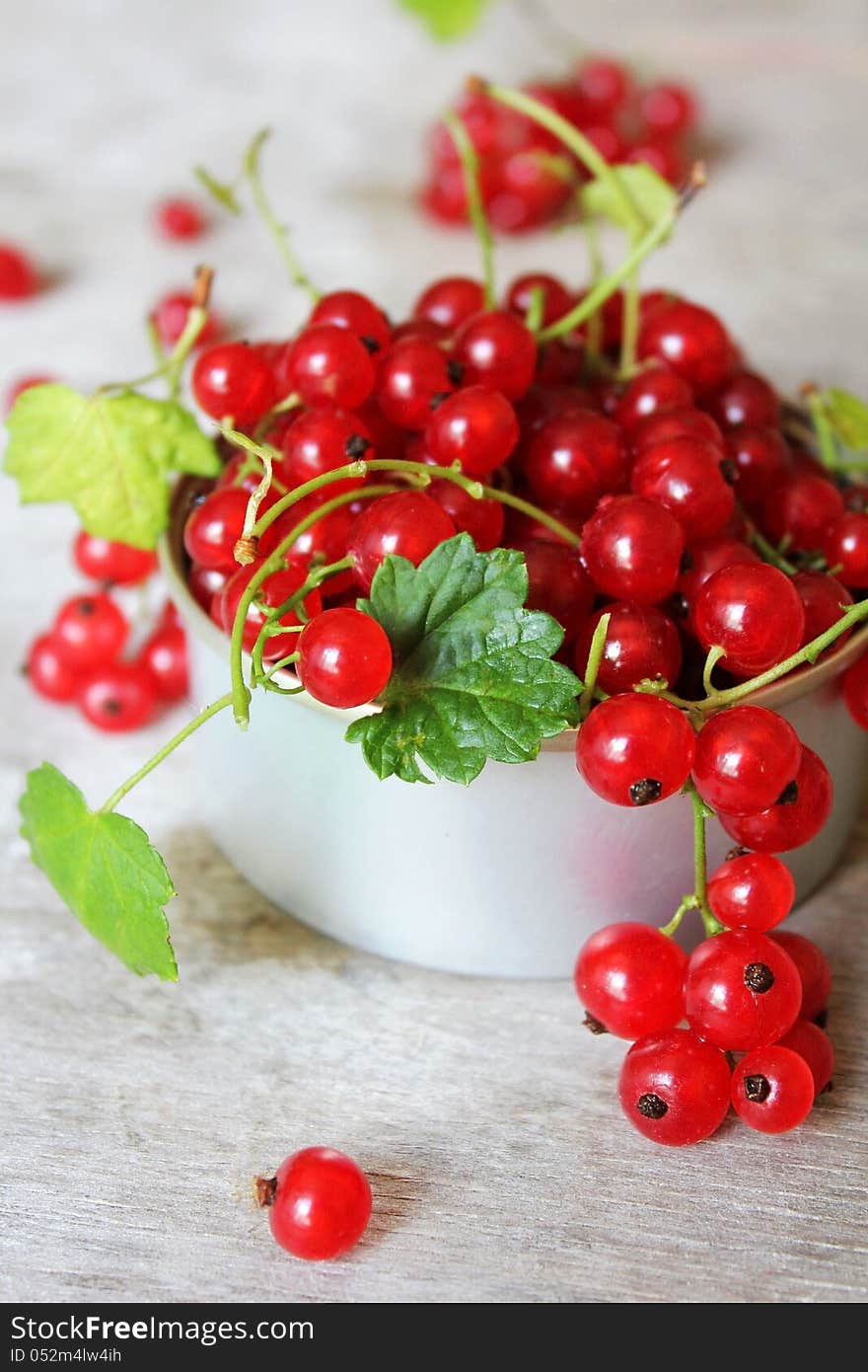 Red currant berries with green leaves in a cup on a wooden surface