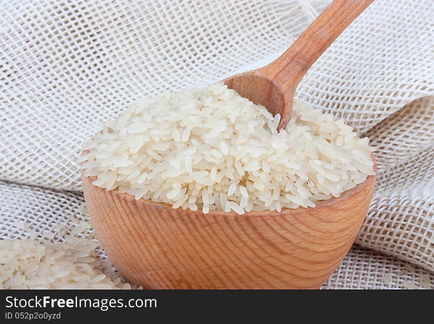 Raw white rice in wooden bowl and spoon on burlap, food ingredient photo