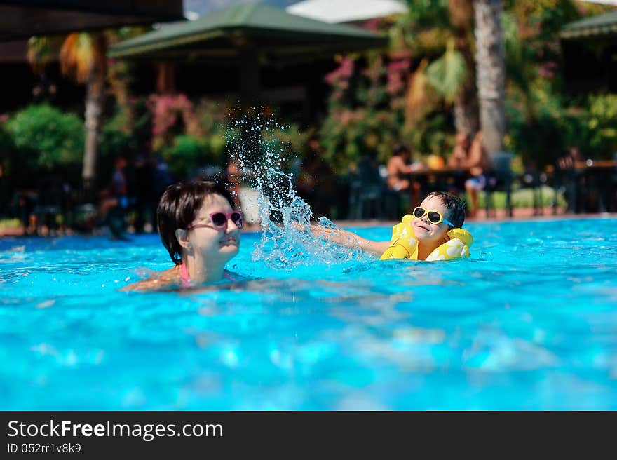 In the sunny day in the summer the boy in sun glasses and in a life jacket plays pool with mum. In the sunny day in the summer the boy in sun glasses and in a life jacket plays pool with mum