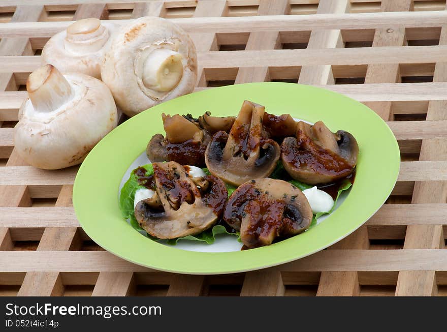 Perfect Grilled Mushrooms Champignons with Grill Sause, Lettuce and Sour Cream on Green Plate closeup on Wood background and Raw Mushrooms. Perfect Grilled Mushrooms Champignons with Grill Sause, Lettuce and Sour Cream on Green Plate closeup on Wood background and Raw Mushrooms