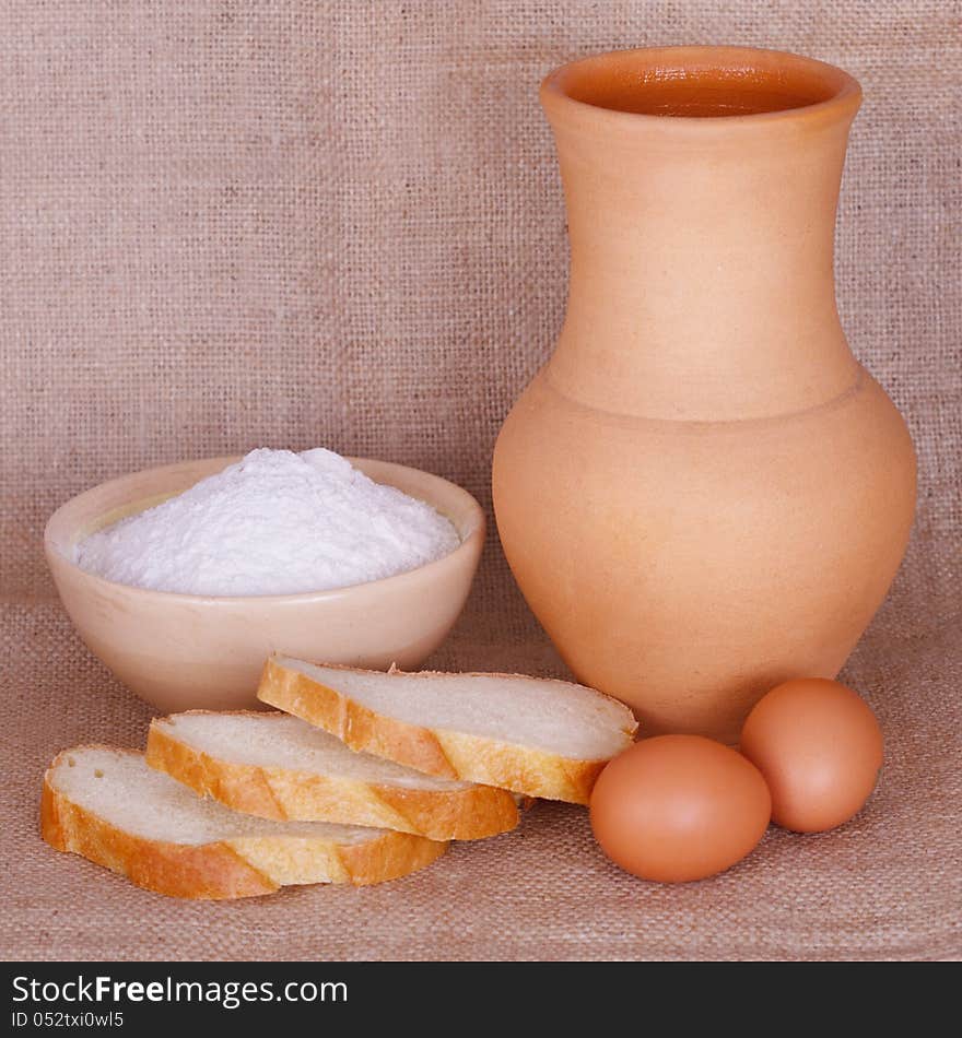 Flour, bread and a pitcher against of burlap