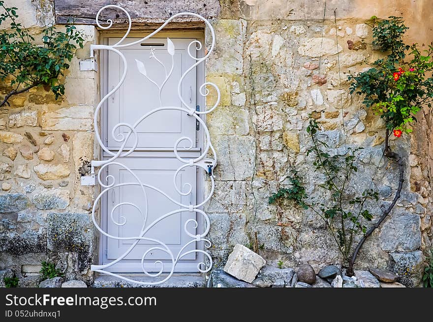 Provence white door in brick wall with metal bars, flowers on the wall. Provence white door in brick wall with metal bars, flowers on the wall