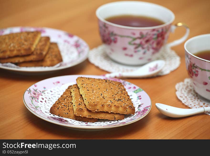 Cookies served with tea in pink china cups with floral pattern on a wooden table. Cookies served with tea in pink china cups with floral pattern on a wooden table