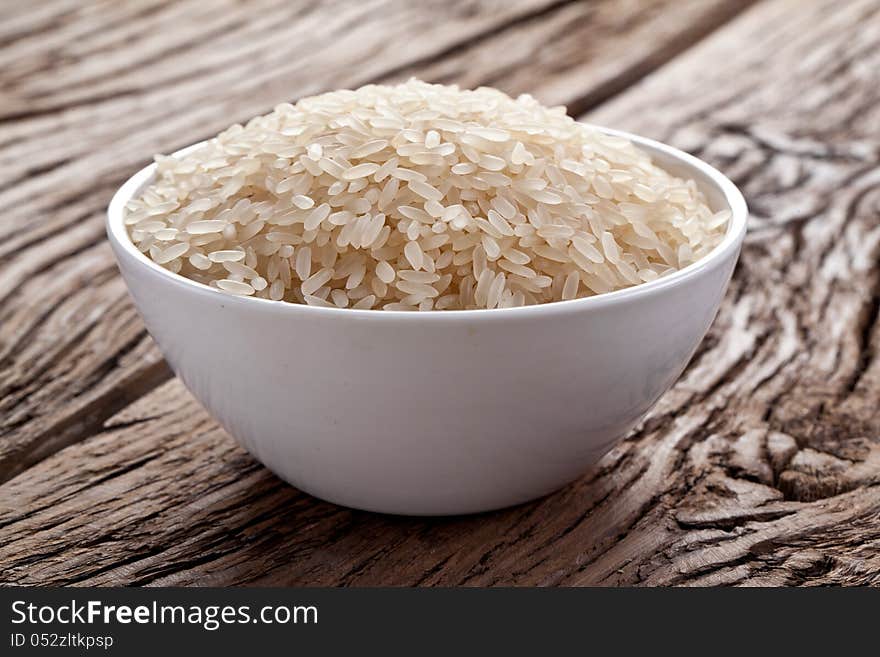 Uncooked rice in a bowl on a dark wooden table.