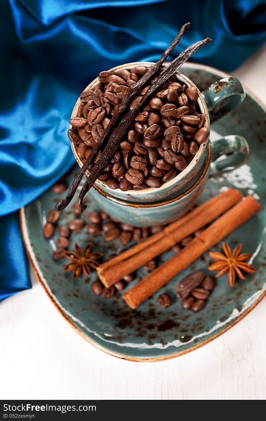 Coffee beans with cinnamon and vanilla in a blue cup on a vintage board