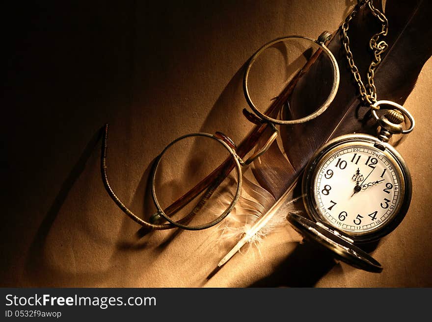 Feather near old spectacles and watch on paper surface under beam of light. Feather near old spectacles and watch on paper surface under beam of light