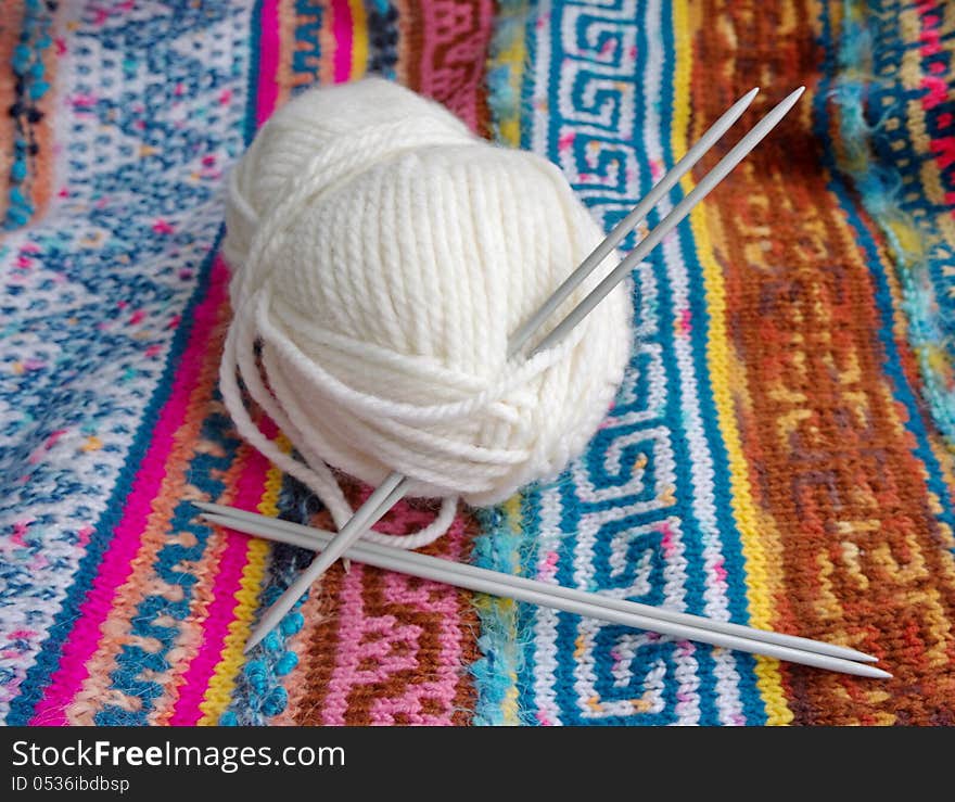 Tangle of white yarn with the knitting needles on the knitted  patterned fabric. Tangle of white yarn with the knitting needles on the knitted  patterned fabric.