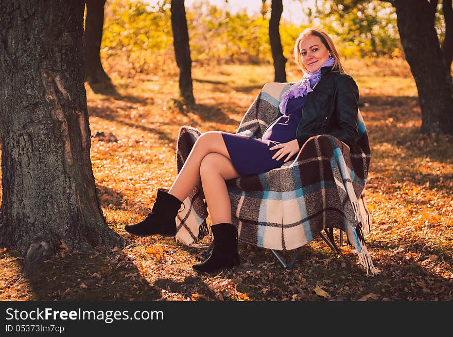 Young pregnant woman sitting on armchair in autumn forest. Young pregnant woman sitting on armchair in autumn forest