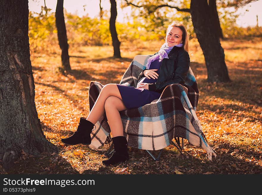 Young pregnant woman sitting on armchair in autumn forest. Young pregnant woman sitting on armchair in autumn forest