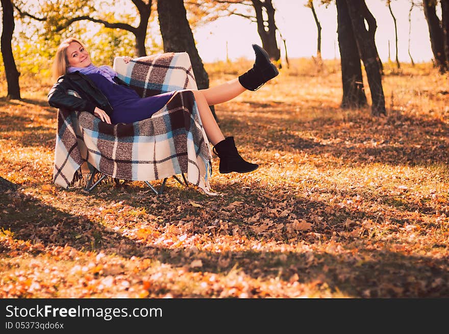 Young pregnant woman sitting on armchair in autumn forest. Young pregnant woman sitting on armchair in autumn forest