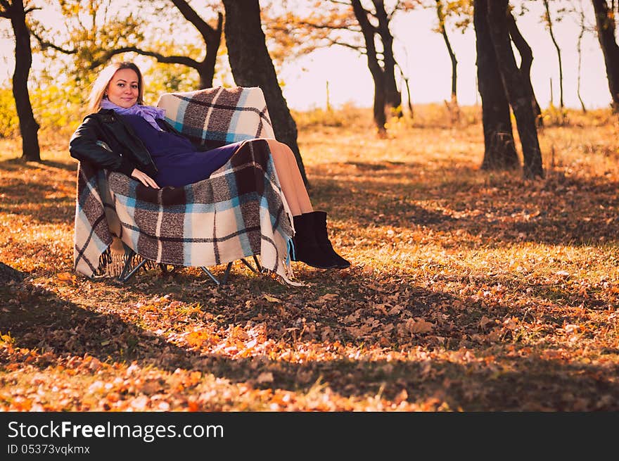 Young pregnant woman sitting on armchair in autumn forest. Young pregnant woman sitting on armchair in autumn forest