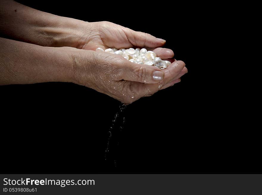 Pearls in female palms of old woman isolated on black background. Pearls in female palms of old woman isolated on black background