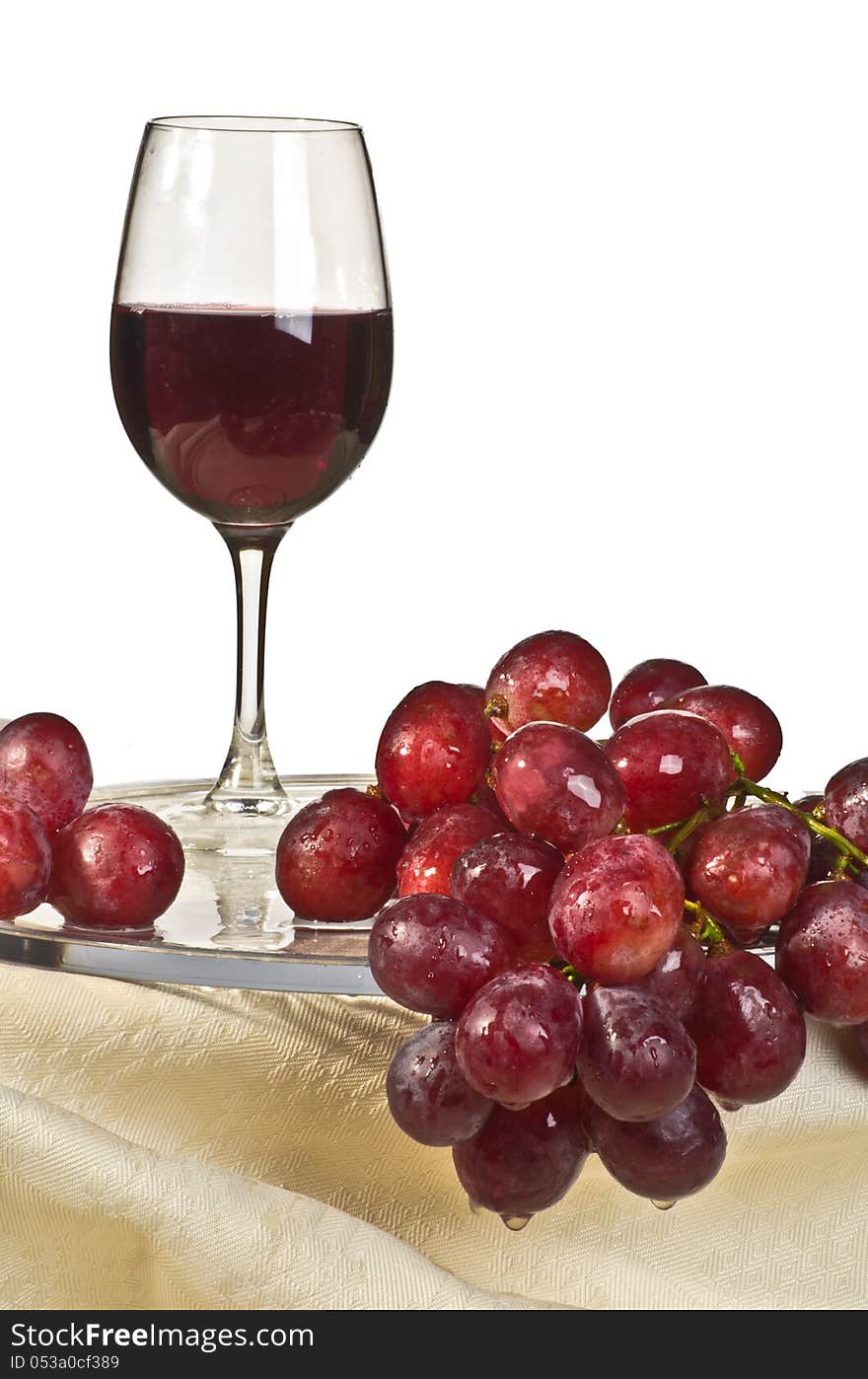 A bunch of red grapes on a glass plate and a glass of wine. A bunch of red grapes on a glass plate and a glass of wine