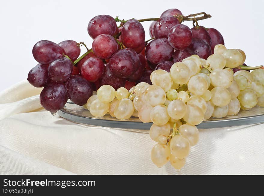 On a large glass dish are ripe grapes: red and white. On a large glass dish are ripe grapes: red and white.