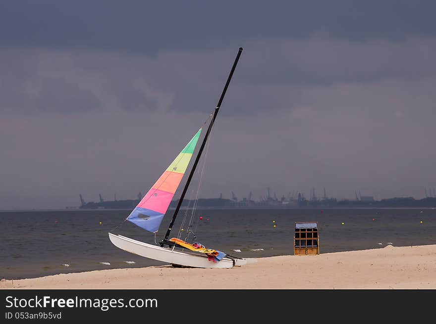 Colorful sailboat on the beach in Sopot, Poland, with the stormy clouds and Gdansk Shipyard in the background.