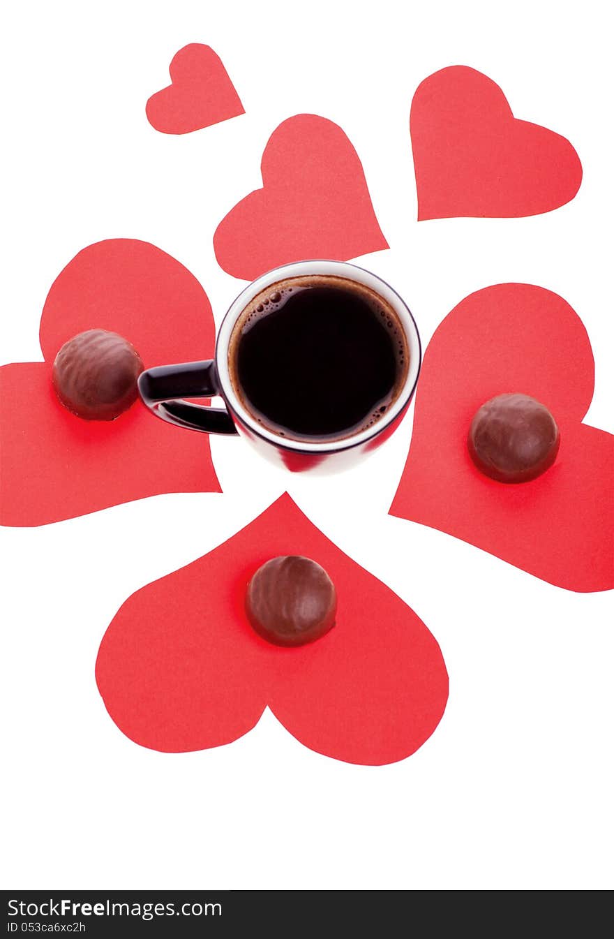 Round chocolate candy in the heart of red paper and black coffee on a white background. Round chocolate candy in the heart of red paper and black coffee on a white background