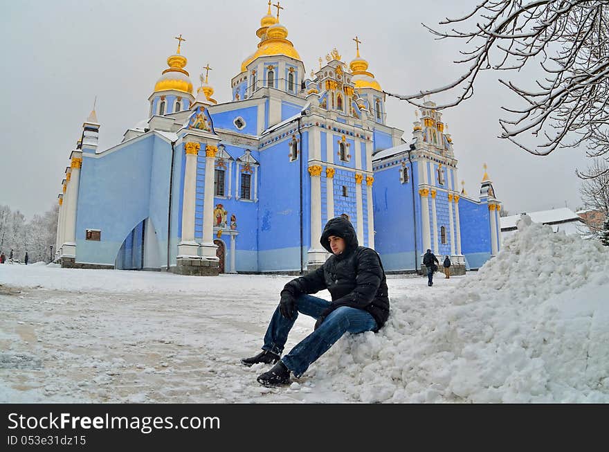 Against church with gold domes the young man in the winter sits. Against church with gold domes the young man in the winter sits