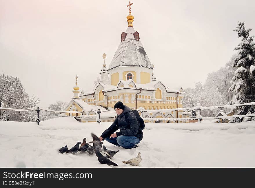 Against a temple with gold domes the person feeds birds. Against a temple with gold domes the person feeds birds