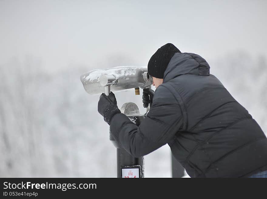 Winter man in a black jacket and hat looking through binoculars. Winter man in a black jacket and hat looking through binoculars