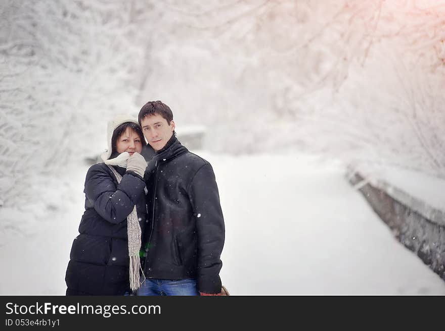 On winter park under a strong snowfall the young pair walks. On winter park under a strong snowfall the young pair walks