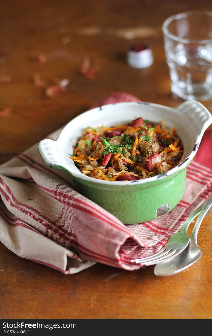 Hot pot of stewed white cabbage with carrots, tomato sauce, sausages and green lentil in a green sauce pan ready to serve