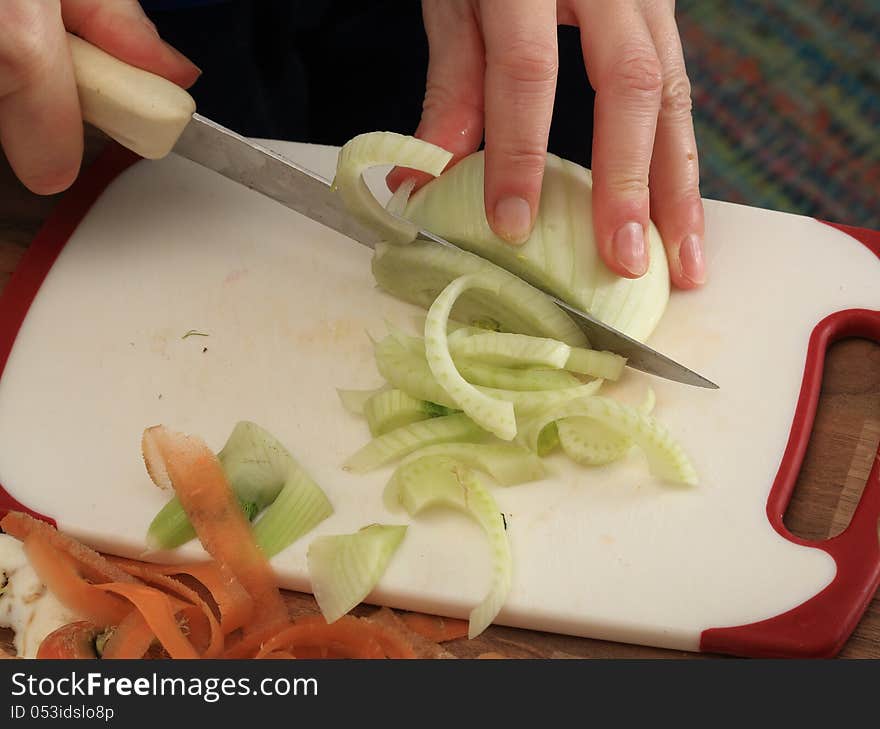 A piece of fennel is cut in thin stripes in order to make a vegetable stew. A piece of fennel is cut in thin stripes in order to make a vegetable stew