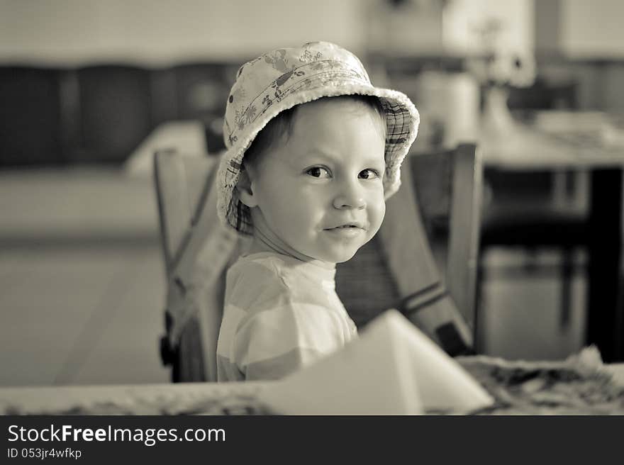 In the room at the table sits a boy in a hat. In the room at the table sits a boy in a hat