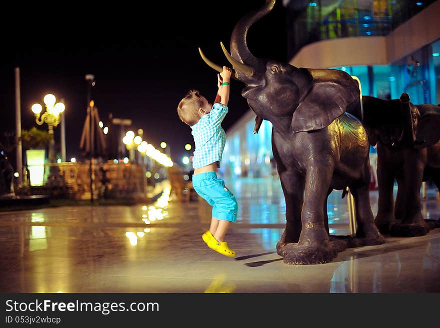 In the evening on the street a boy playing with an elephant sculpture. In the evening on the street a boy playing with an elephant sculpture