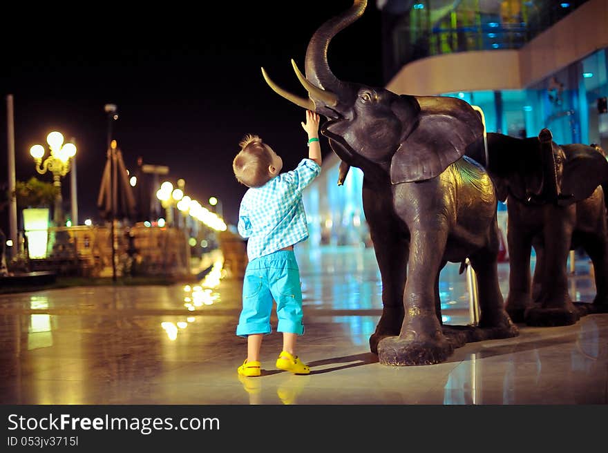 In the evening on the street a boy playing with an elephant sculpture. In the evening on the street a boy playing with an elephant sculpture