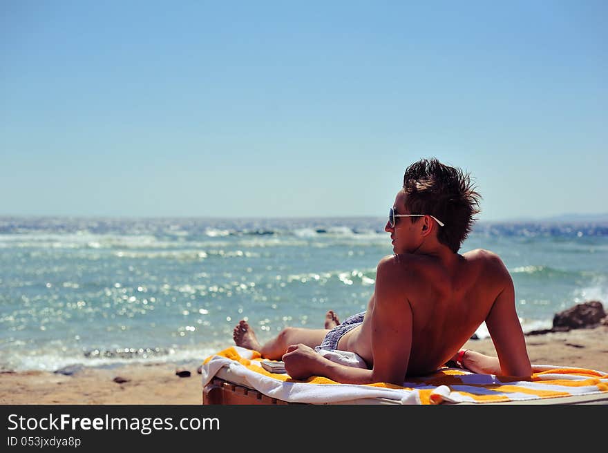 The young man has a rest on a beach against sparkling ocean. The young man has a rest on a beach against sparkling ocean