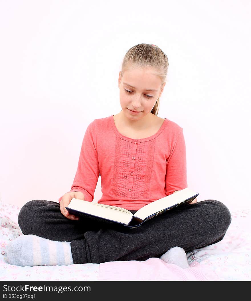 Blond Girl Reads Interesting Book Sitting On Bed